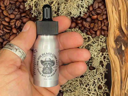 Close-up of a premium aluminum dropper bottle labeled "Cowboy Crush GOOD BOY Beard Oil" by Big Dog Beard Company, showcasing an elegant design and rich, warm hues that hint at the luxurious blend of Cedarwood, Black Pepper, Oakmoss, and Coffee within.